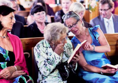 Hochzeitsgäste in der Kirchenbank, eine ältere Dame lacht