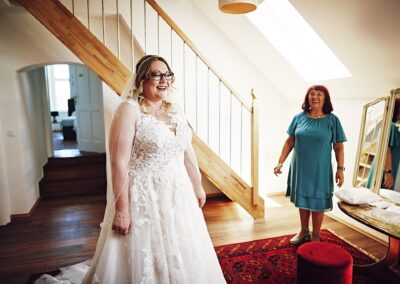 Braut im Treppenhaus, eine Frau im blauen Kleid schaut ihr zu