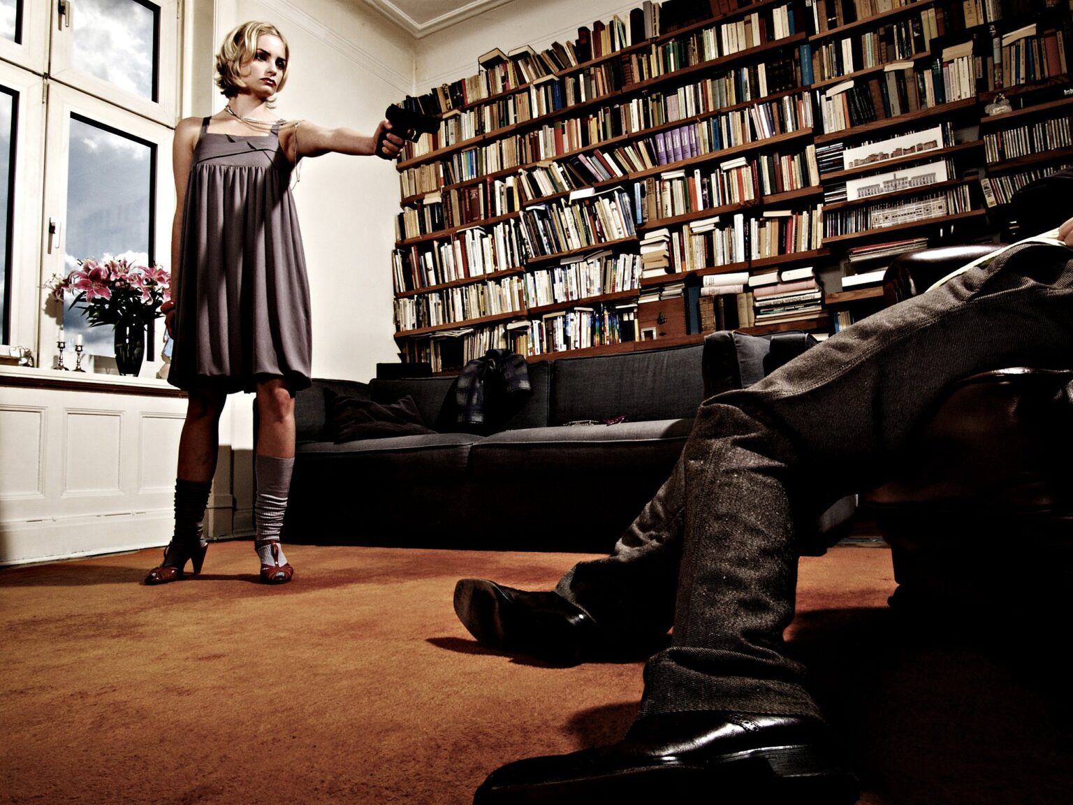 Modefotografie aus der Serie Fashion Victims: Frau steht in einer Bibliothek, am Boden liegt ein Mann
