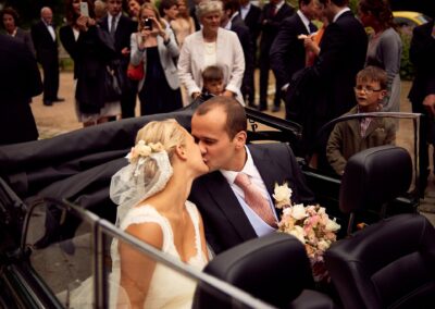 Brautpaar küsst sich im Cabrio, umringt von Gästen – Hochzeit in Hamburg