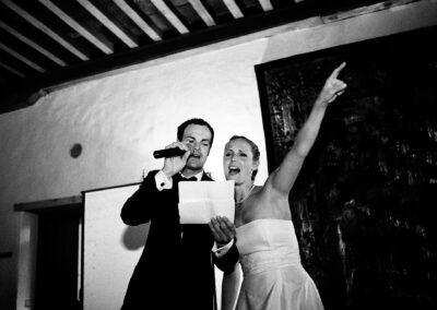 Brautpaar bei einer Rede am Abend, die Braut zeigt lachend nach oben, schwarzweiß – Hochzeit in Hamburg