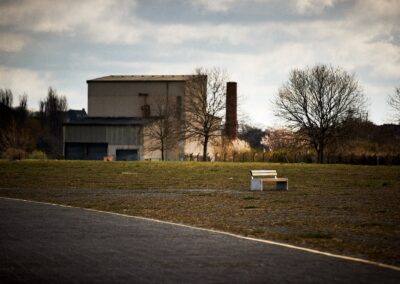 Wiese und Weg vor einem alten Industriegebäude unter Wolkenhimmel