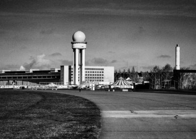 Radarturm und Flughafengebäude am Rand eines ehemaligen Flugfelds, schwarzweiß