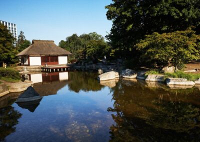 Pavillon spiegelt sich in einem Parkteich unter blauem Himmel