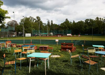 Bunte Stühle und Tische auf einer Wiese vor einem Sportplatz