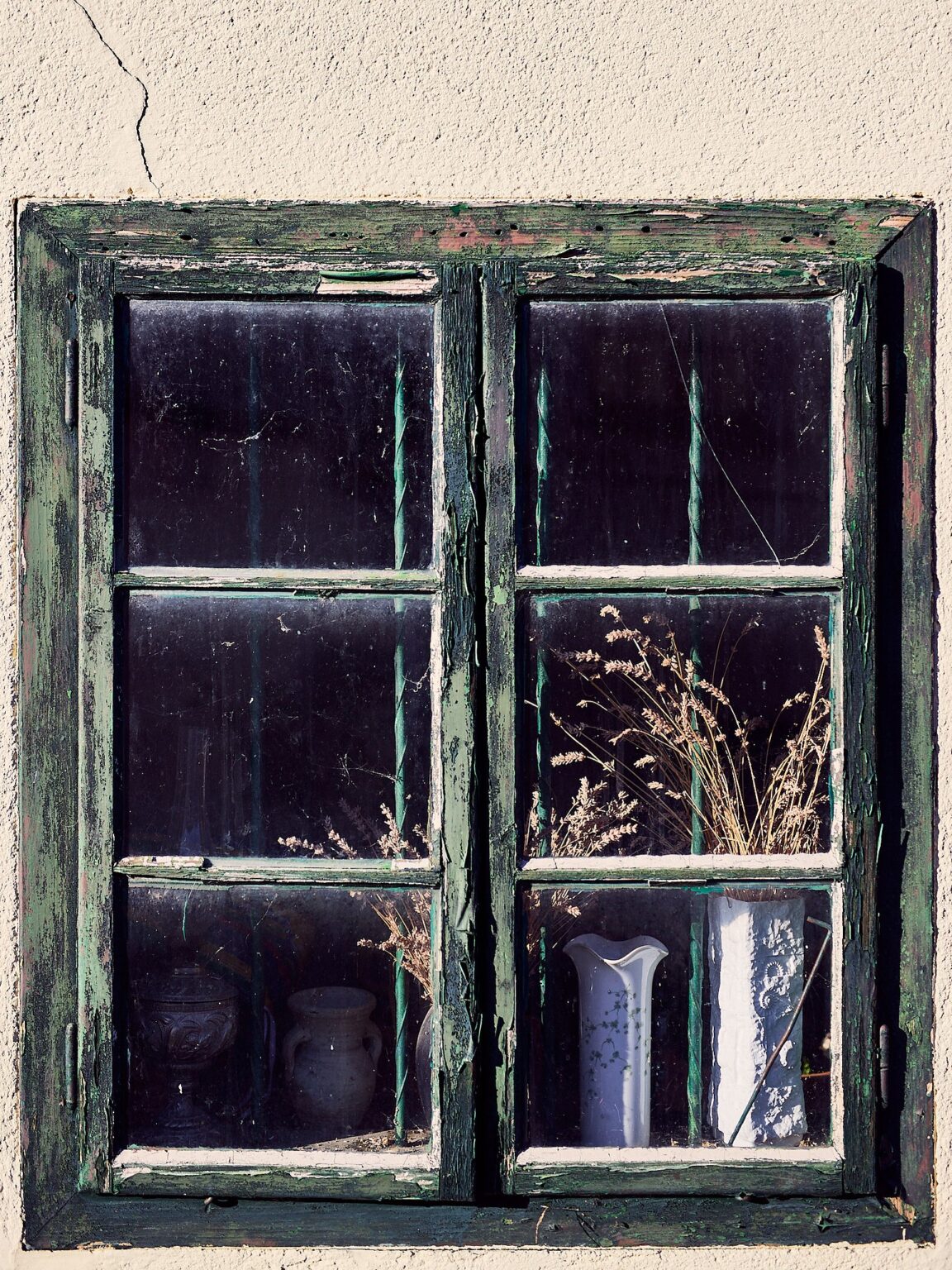 Altes Holzfenster mit Trockenblumen und Vasen dahinter